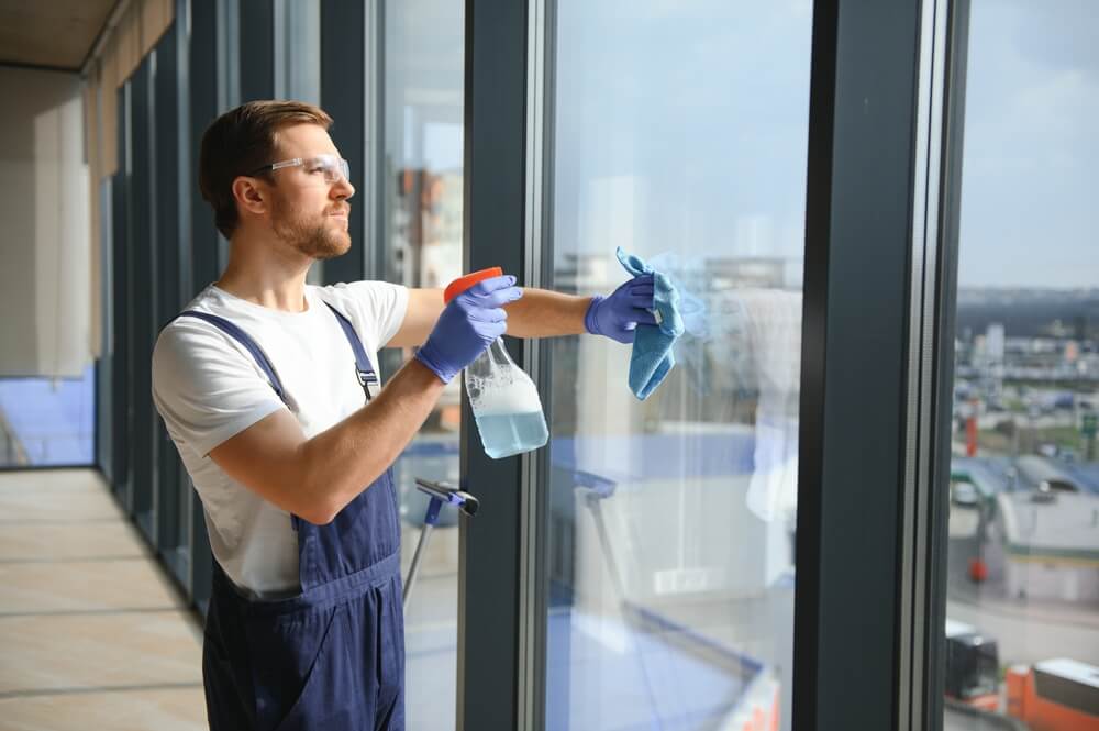 Un employé d'un service de nettoyage professionnel lave la vitre des fenêtres du bâtiment.