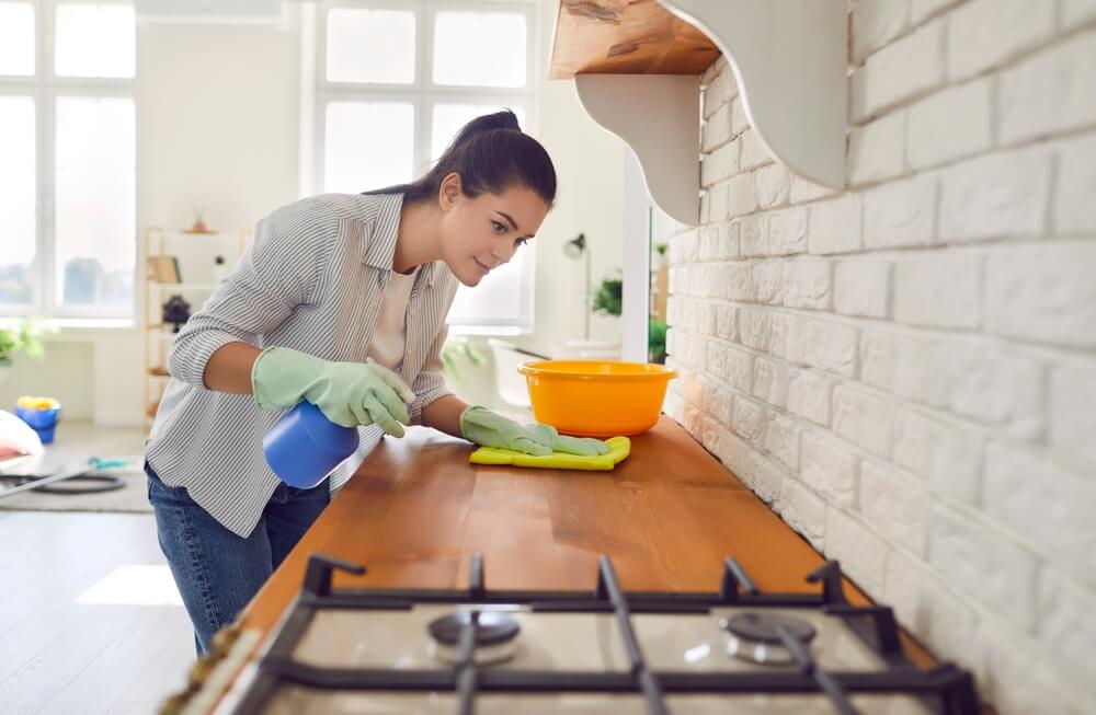 Jeune femme au foyer portant des gants de protection en caoutchouc dans la table de travail moderne de la cuisine, en utilisant du chiffon et des vaporisateurs de détergent efficaces, les services ménagers, les services de nettoyage, les travaux domestiques, l'entretien ménager.