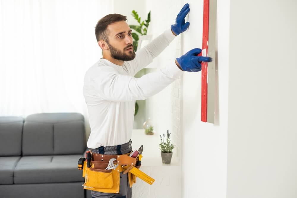 Homme plâtrier ouvrier de construction au travail, prend le plâtre du seau et le met sur la truelle à plâtrage du mur, porte un casque à l'intérieur du chantier d'une maison.
